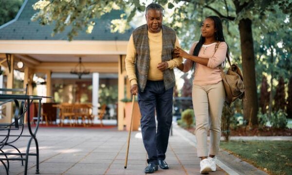 istockphoto-1413584168-612x612 Smiling African American woman walking with her senior father while visiting him at nursing home.